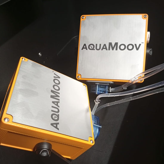 Two AQUAMoov branded orange and silver square boxes connected by clear tubing on a black surface.