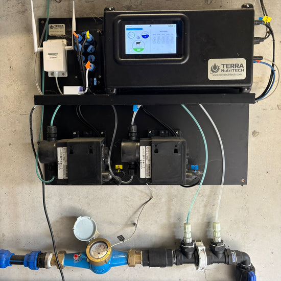 OPISPro precision mineral dosing system mounted on a concrete wall, featuring a digital control unit and dosing pumps connected to mineral and water lines to automatically deliver liquid minerals through the herd’s drinking water. The system can automatically dose up to six mineral blends to three different herds through their drinking water.